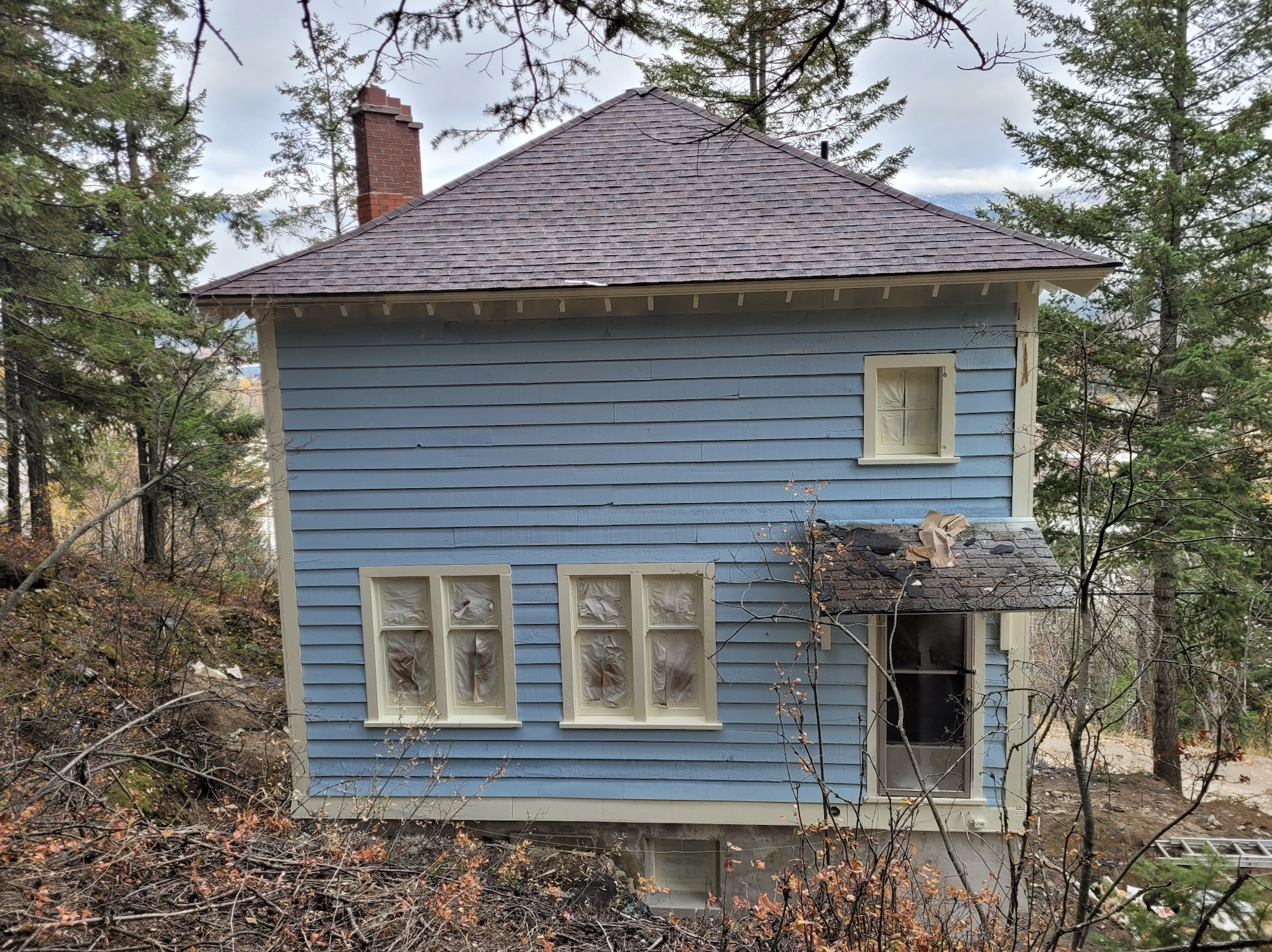 Looking at the front entrance of the blue chalet from the forest hillside, missing its front porch. Taken during documentation and renovations, October 2023. From Capture2Preserv project.